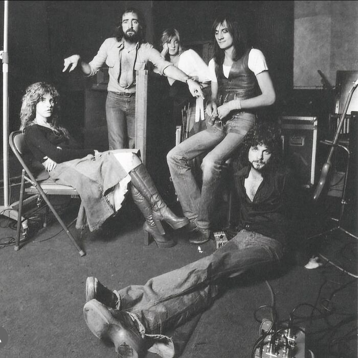 1970s rock legends in a studio setting, casually posing and preparing to create iconic music in a raw, vintage atmosphere.