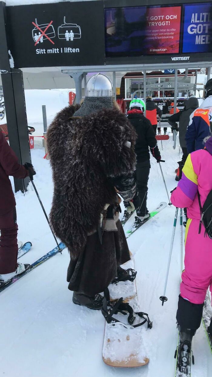 Person wearing Viking costume and helmet snowboarding in a ski lift line showing suspiciously unbothered attitude.