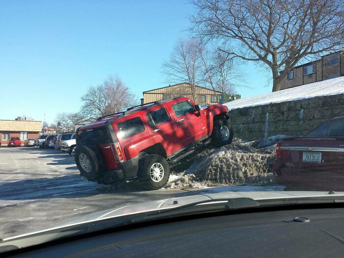 Red SUV parked on a snow mound ignoring parking rules, showing suspiciously unbothered attitude in an urban setting.