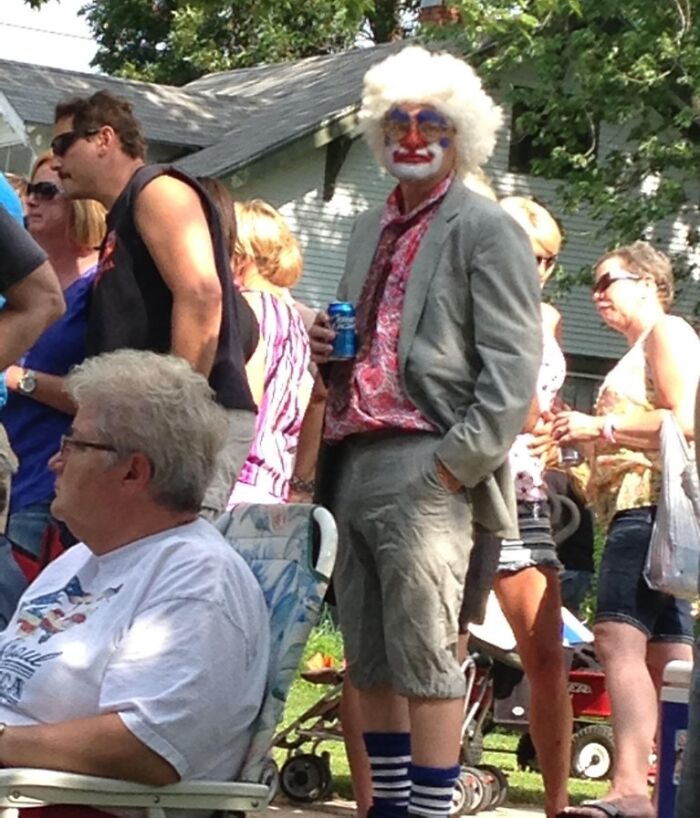 Man dressed as a clown standing unbothered in a crowd, holding a can, showing suspiciously unbothered attitude.