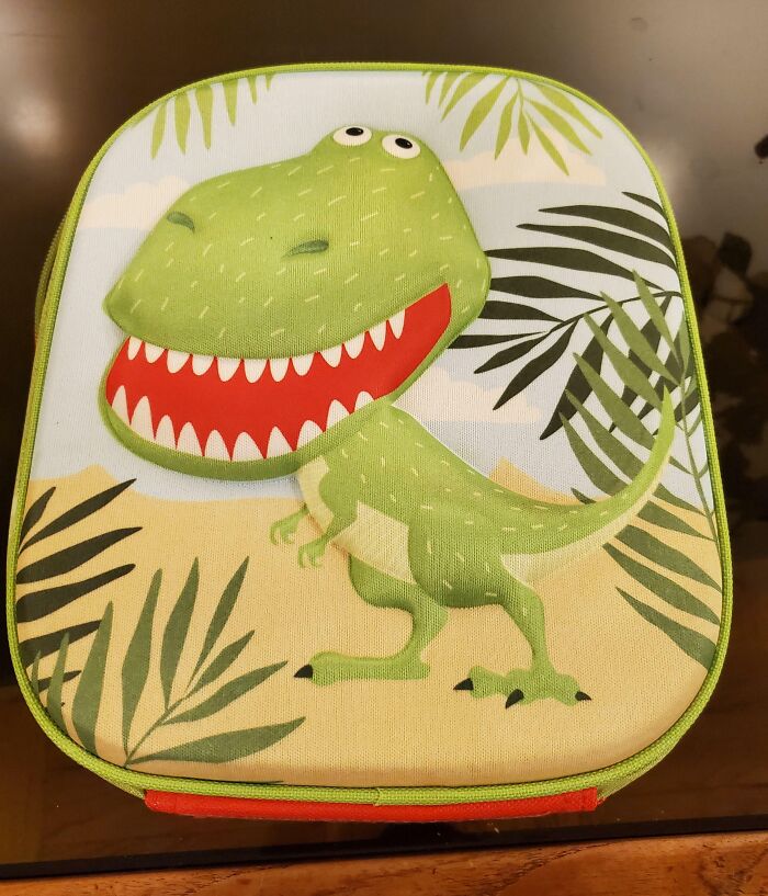 Green cartoon dinosaur with a big smile on a lunchbox, surrounded by leaves in a jungle setting, showing zero ducks given.