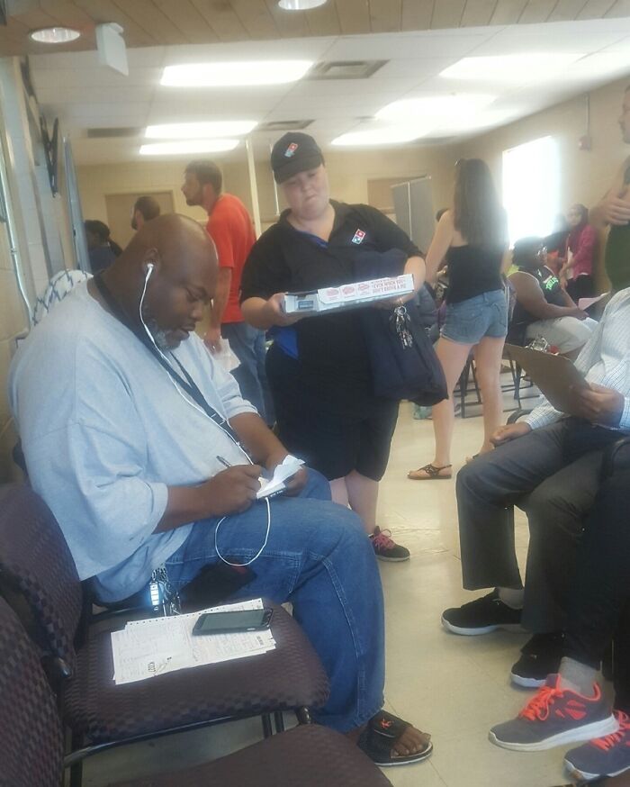 Man wearing headphones and writing while a delivery worker stands nearby showing zero concern in a crowded room.