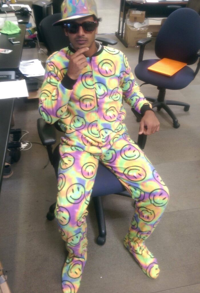 Man wearing colorful smiley face outfit and hat, sitting relaxed in office chair showing suspiciously unbothered attitude.