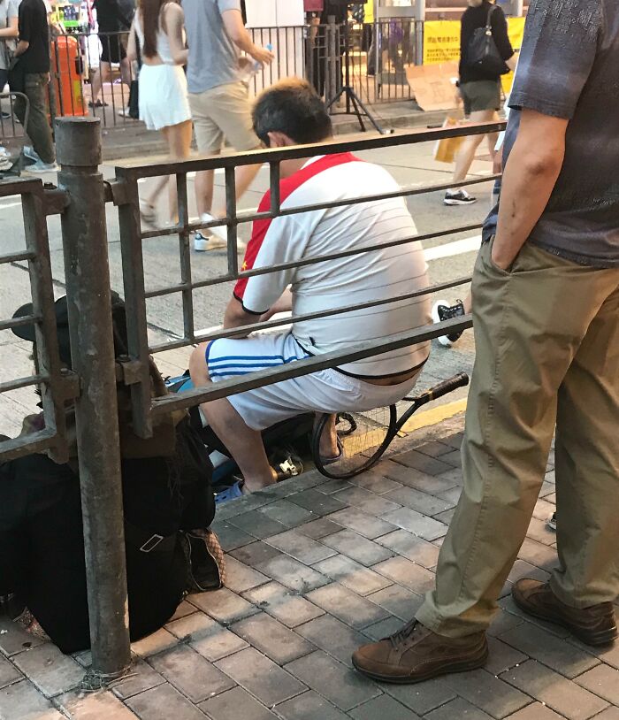 Man sitting on the ground unbothered by surroundings while people walk past on a busy street sidewalk.