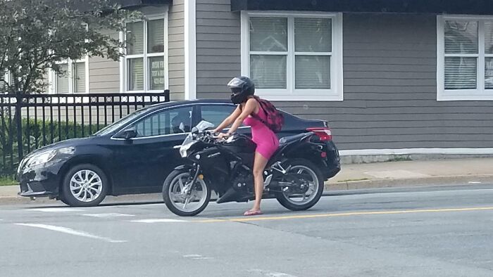 Person in a bright pink outfit riding a motorcycle, looking suspiciously unbothered and unconcerned on a city street.