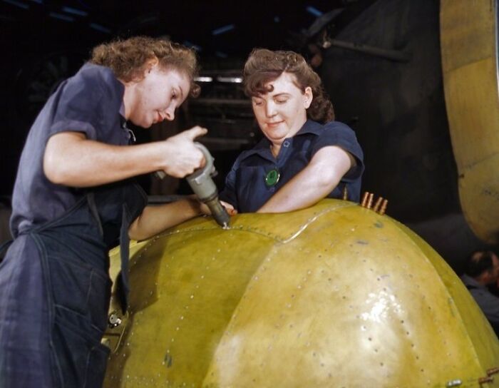 Women at work during WWII using tools to assemble aircraft parts in a factory setting focused on manufacturing.