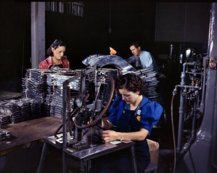 Women at work during WWII operating industrial machinery and assembling metal parts in a factory setting.