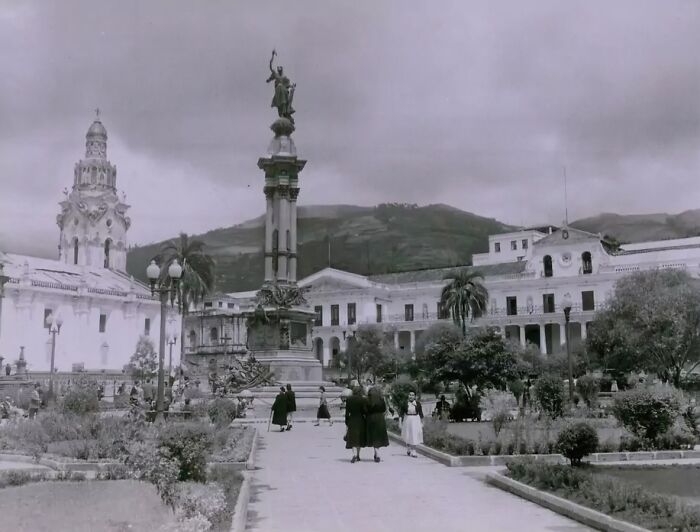 Black and white photo of daily life in the 50s showing people walking near a historic plaza and monument.