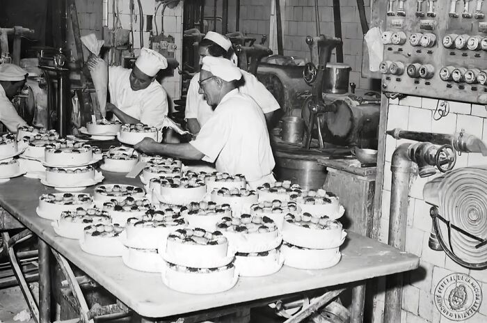 Black and white photo of bakers preparing cakes in a bakery, showcasing daily life across the globe in the 50s.