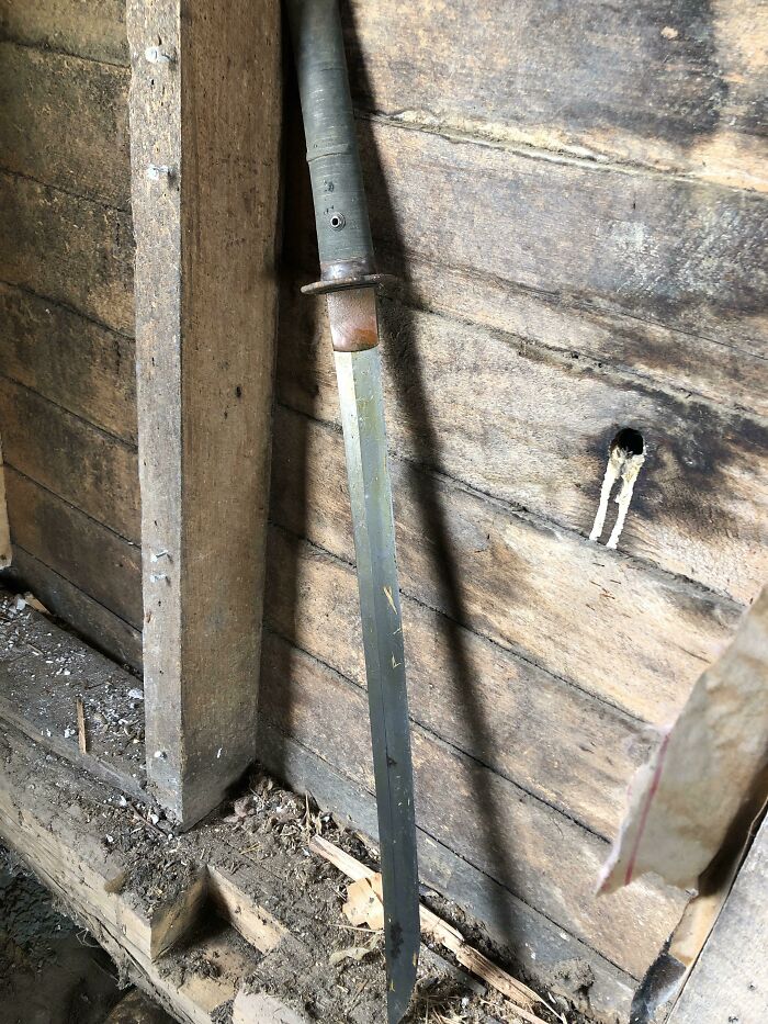 Old rusty bayonet found hidden under floor boards in an abandoned wooden home with dusty debris around.