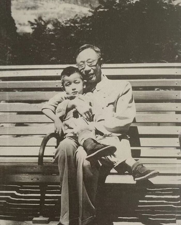 Black and white photo of a man holding a child on a bench, capturing daily life across the globe in the 50s.