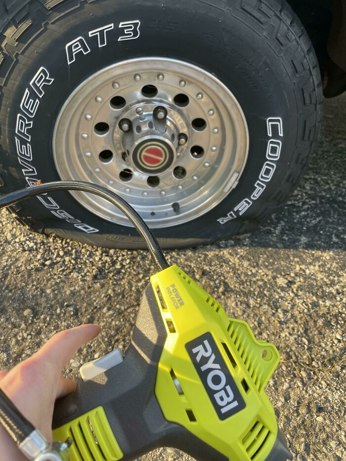Hand holding a Ryobi power inflator near a Cooper tire, demonstrating calm tire inflation skills outdoors.