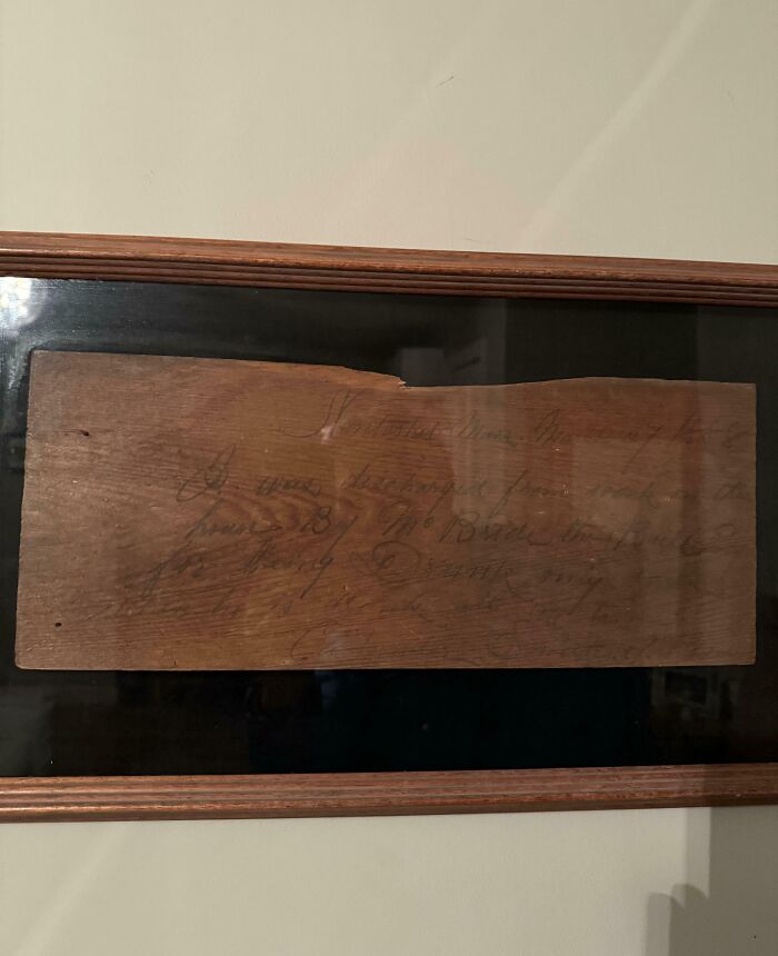 Fossil under old floorboards framed on wall, showing aged wood with faint handwritten text visible on surface.