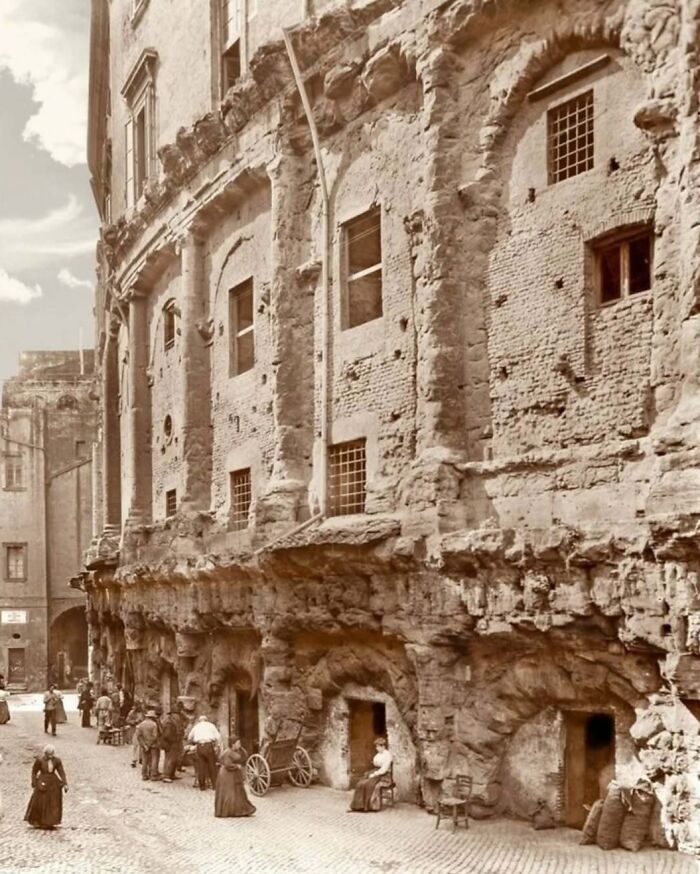 Historic old architecture with weathered stone walls and arches lining a cobblestone street with people walking nearby
