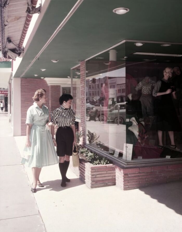 Two women in 1950s attire window shopping on a sunny street, capturing everyday life in 1950s Florida.