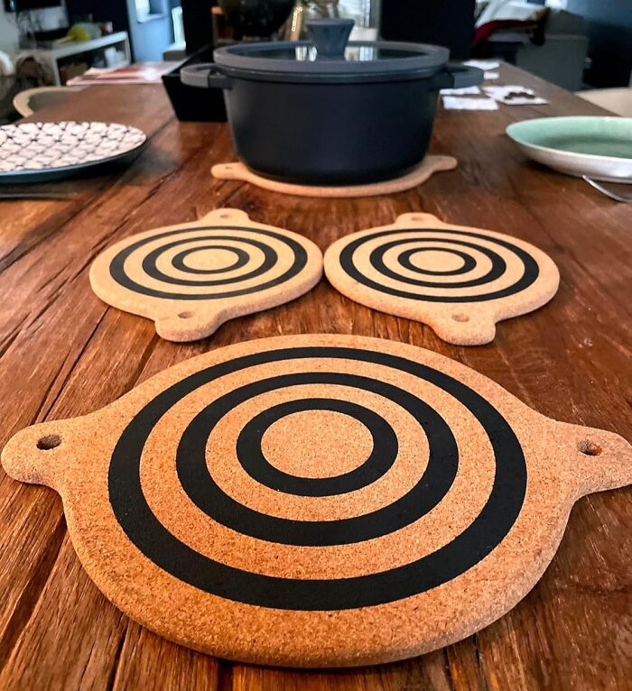 Set of circular cork kitchen items with black concentric ring designs on a wooden countertop near a black pot.