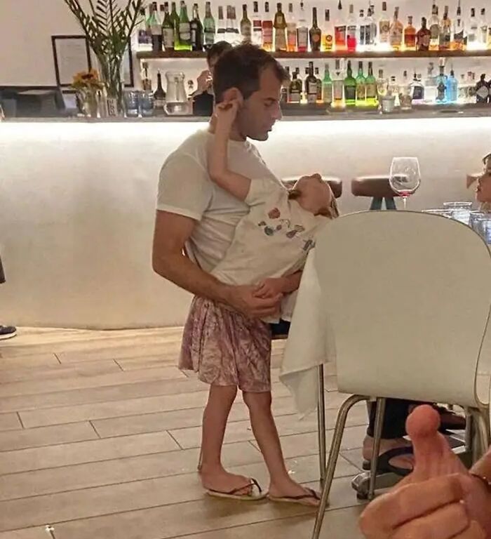 Man holding a child whose legs appear unusually long in a cursed image with unhinged visual distortion.