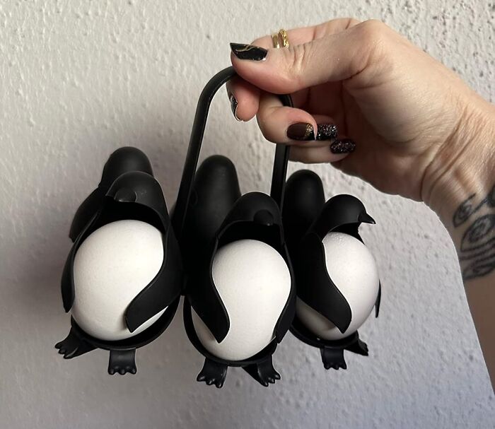 Hand holding a quirky penguin-shaped egg holder, a weird kitchen invention organizing white eggs efficiently.