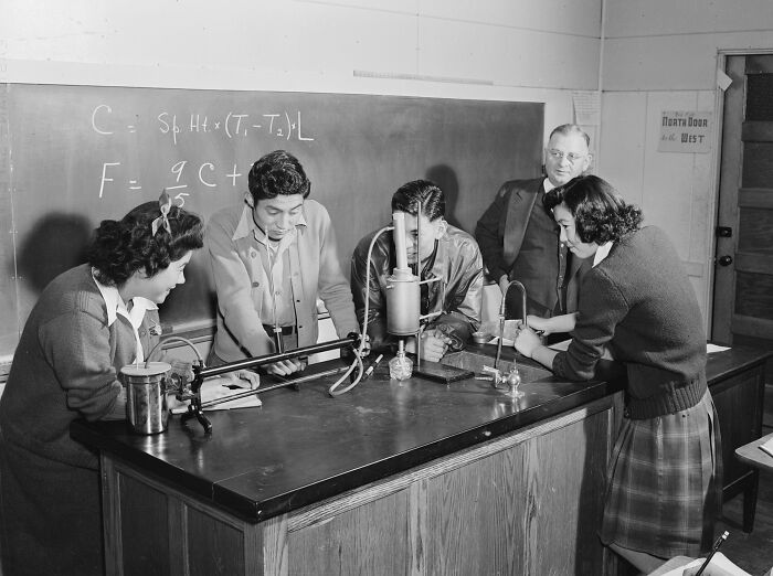 Students conducting a science experiment in a classroom at a school worldwide during World War II, with teacher observing.