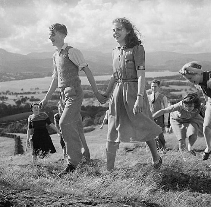 Students from a school during World War II holding hands and walking outdoors in a scenic countryside setting.