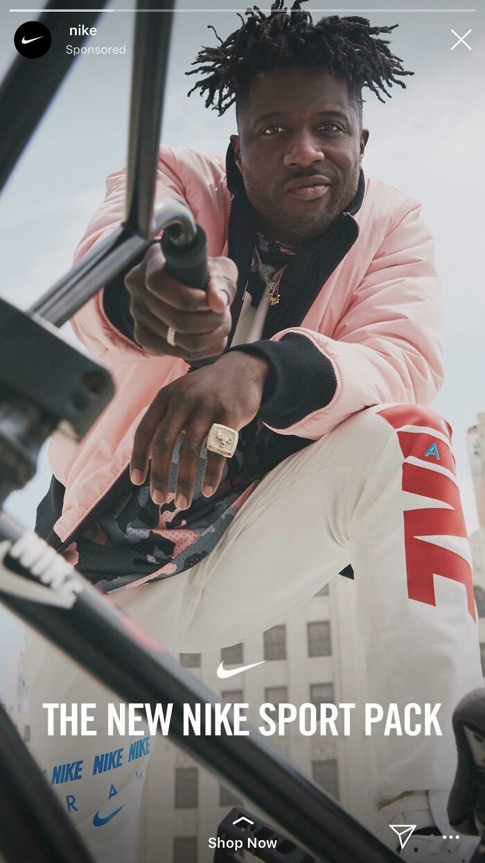 Man wearing pink jacket and white Nike pants posing with bicycle in urban setting for advertising fails.