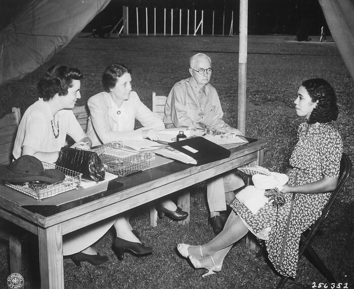 Black and white image of a school interview outdoors with teachers and a student during World War II era.