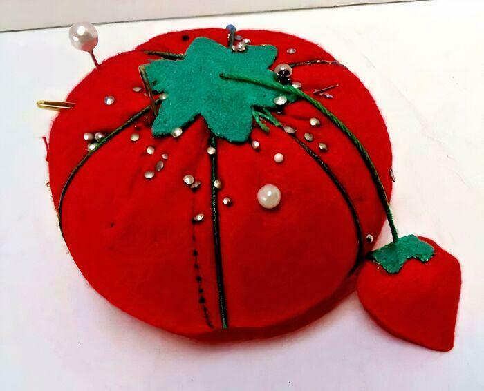 Red tomato-shaped pincushion with pins and attached small strawberry, nostalgic vintage sewing accessory.