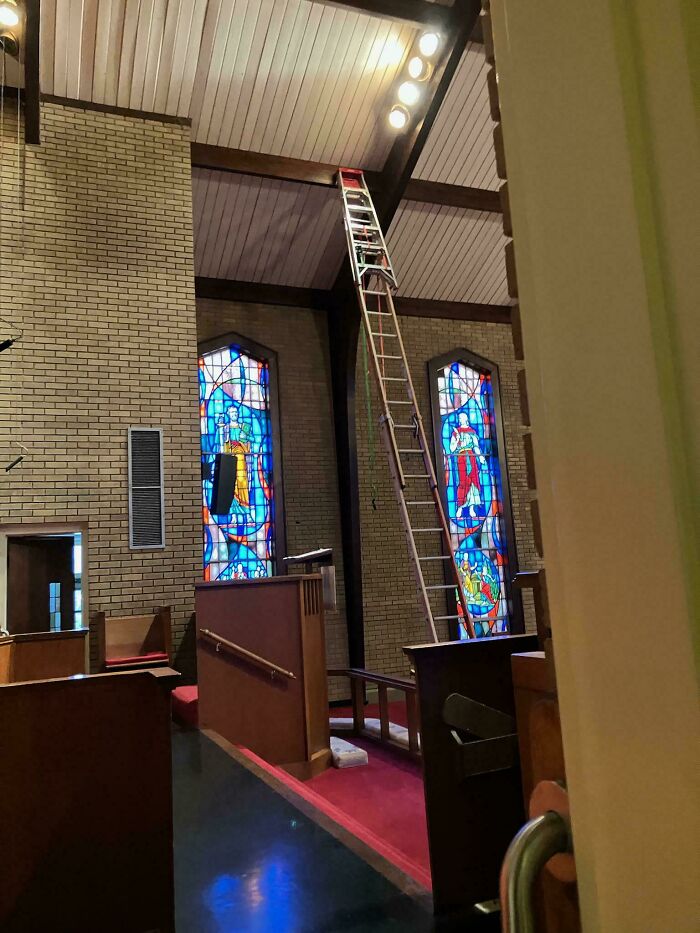 Tall unsecured ladder inside a church near stained glass windows showing employees ignoring safety protocol risks.