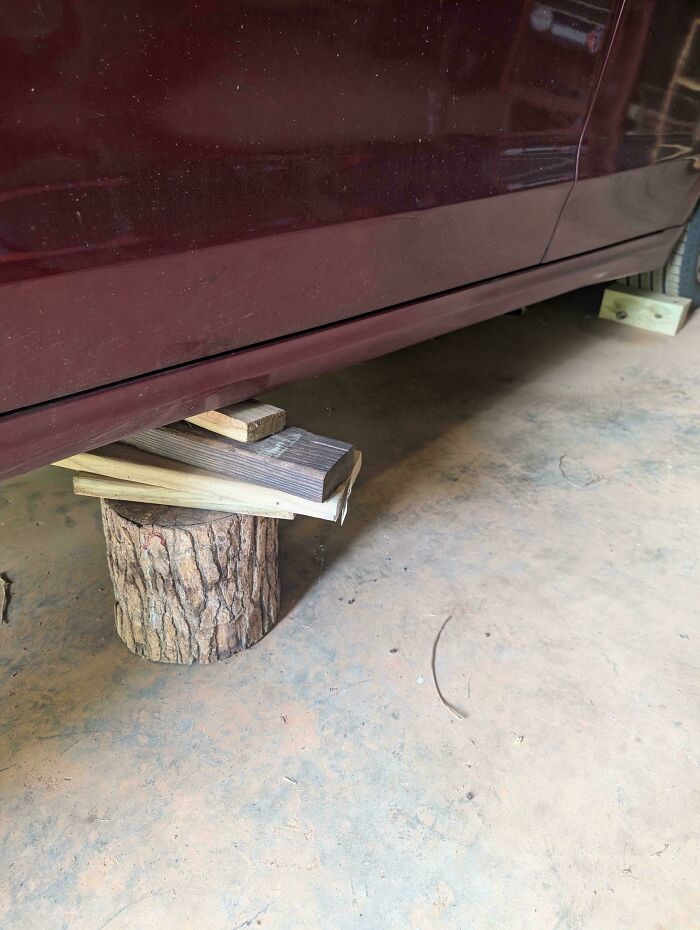 Car dangerously supported by unstable wood and log, ignoring safety protocol in a risky makeshift setup.