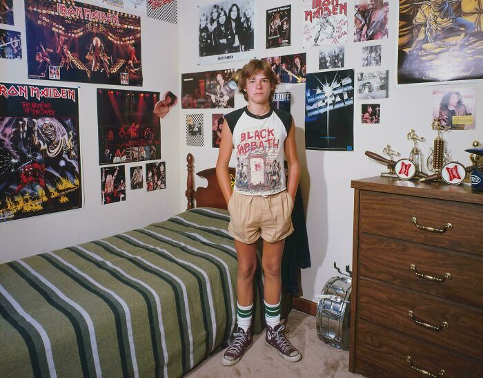 Teenager standing in a bedroom filled with classic rock band posters, showcasing candid glimpses into the past.