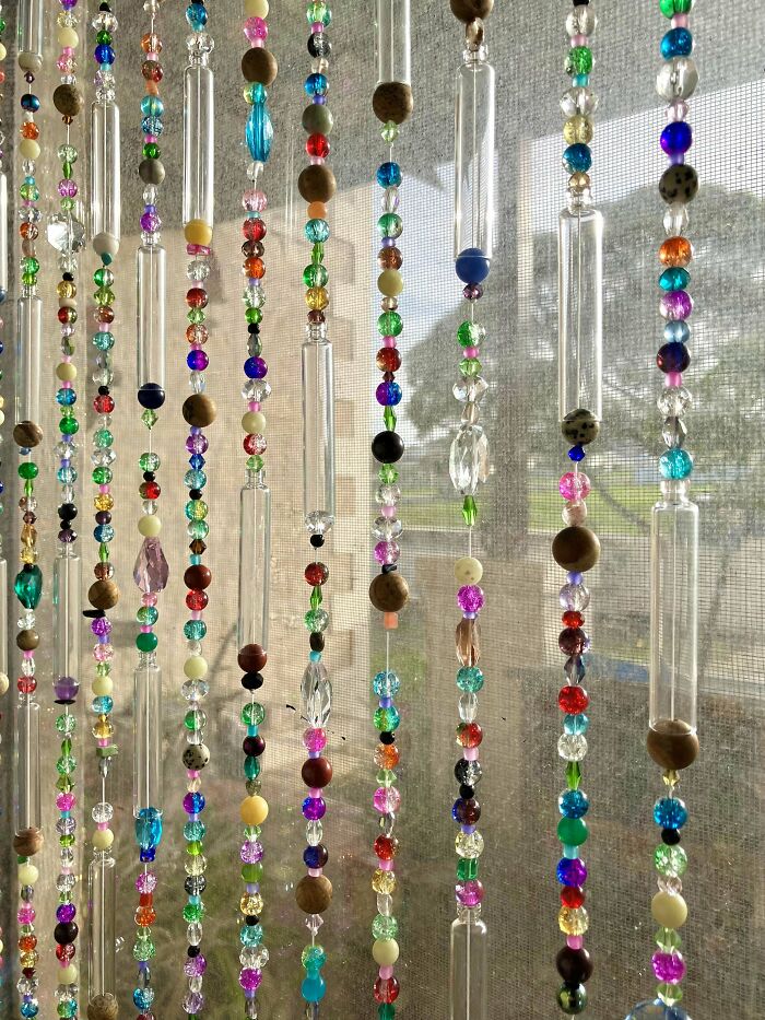 Colorful handmade beaded curtain with glass and wooden beads hanging in front of a window with sunlight.