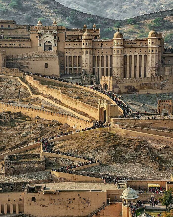 Ancient fort with impressive architectural feats featuring large walls, arched gates, and a winding pathway filled with visitors.