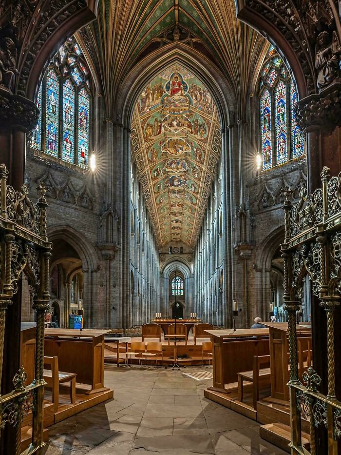 Gothic cathedral interior with vaulted ceilings, stained glass windows, and detailed architectural feats in stone and wood.