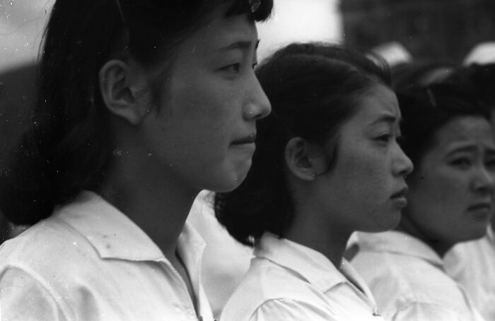 Three young women in white shirts standing in profile during World War II, a historical image of schools worldwide.