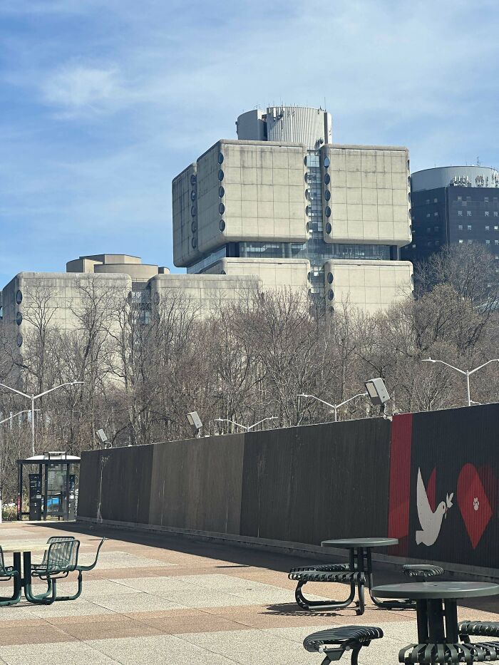 Brutalist evil building with large concrete blocks and round windows behind leafless trees on a clear day.