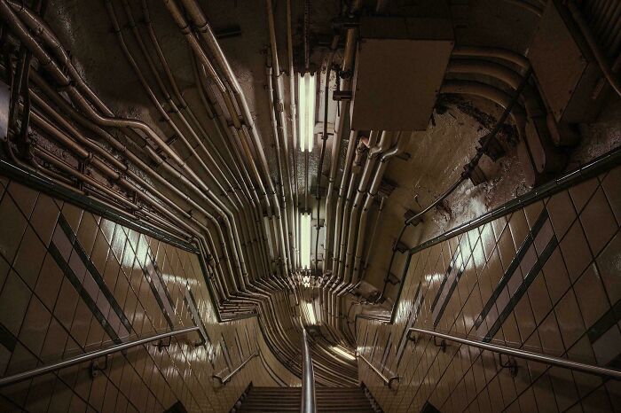Dimly lit stairwell in a building with eerie pipes and tiles, giving an evil building vibe from a horror movie setting.