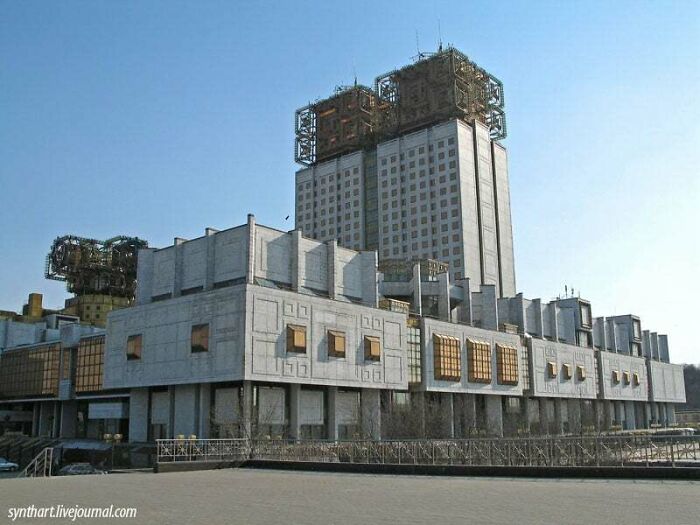 Brutalist evil building with blocky architecture and industrial structures on top under a clear blue sky.