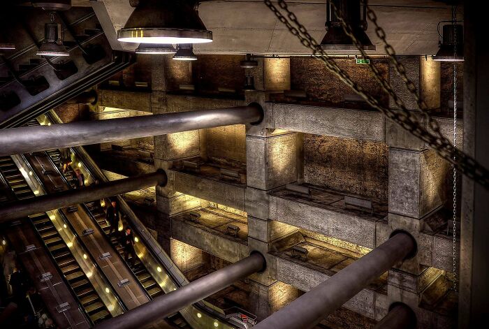 Dark industrial interior of an evil building with large pipes, chains, and escalators evoking a horror movie atmosphere.