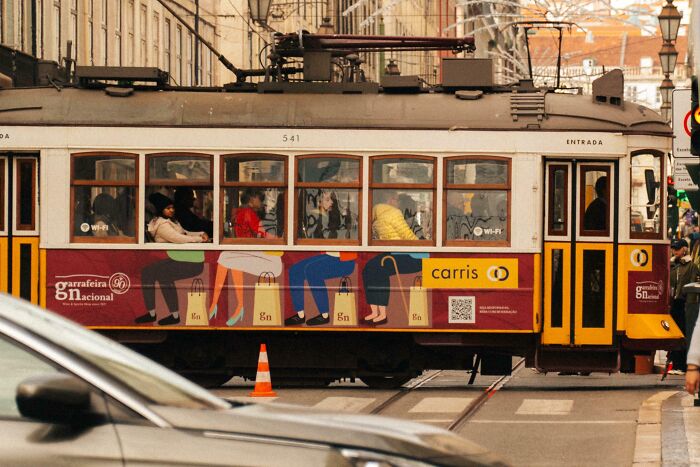 Yellow tram with funny advertising fail showing unrealistic body parts on passengers, moving through a busy city street.