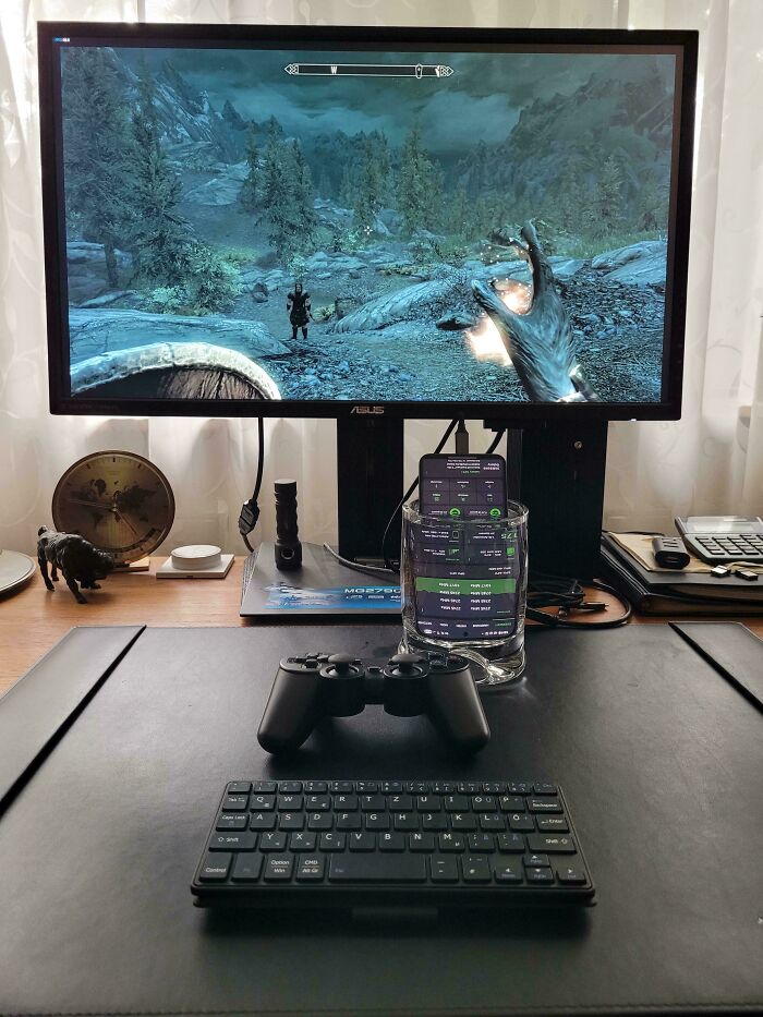 Gaming setup with a smartphone in a glass, controller, and keyboard showcasing redneck engineer creativity and ingenuity.