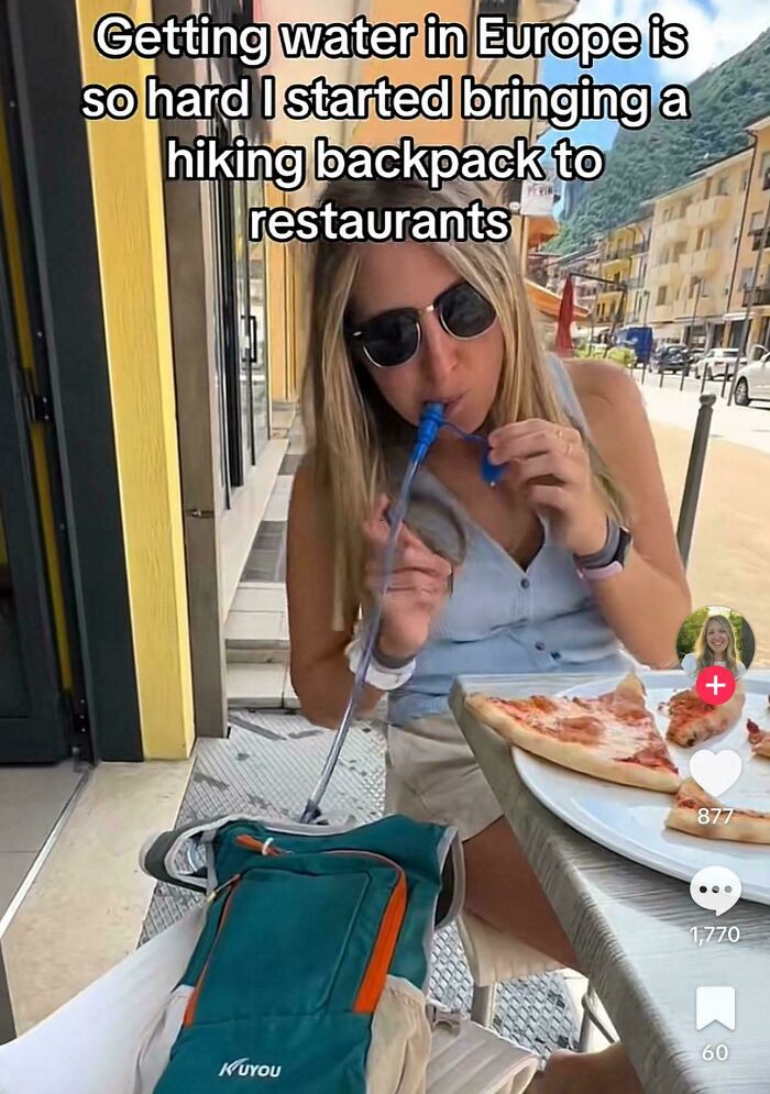 Woman using a hiking backpack hydration system at a restaurant, illustrating funny dumb American posts about daily life.
