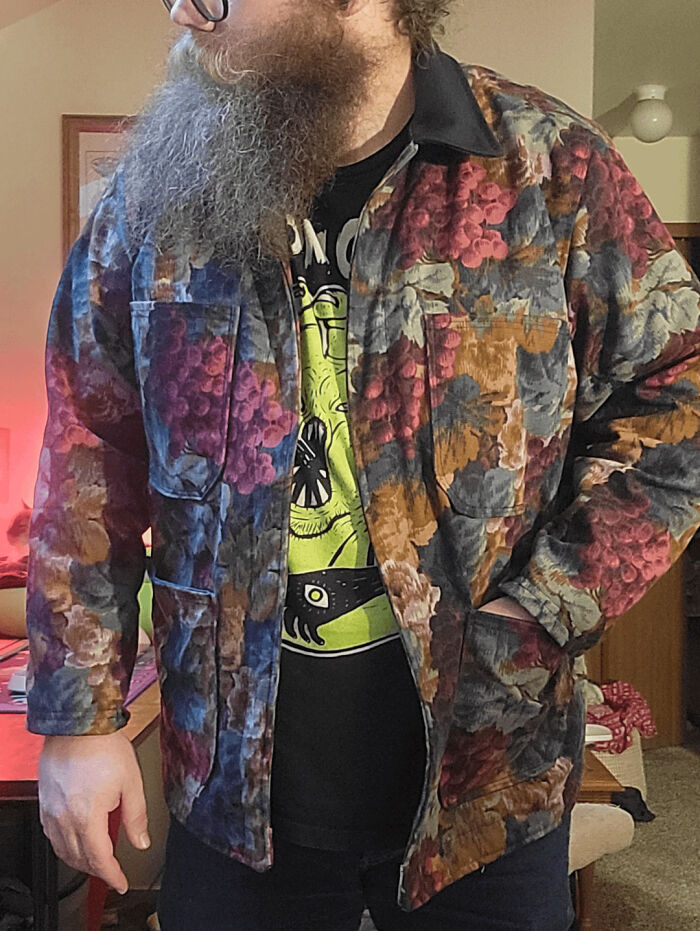 Man with long beard wearing a colorful floral patterned jacket posing indoors, showcasing cool creative clothing design.