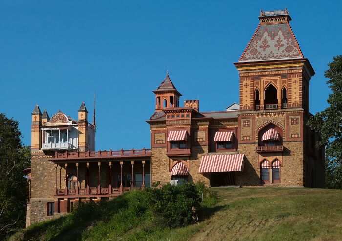 Historic home with intricate brickwork and striped awnings set against a clear blue sky, showcasing American architectural heritage.