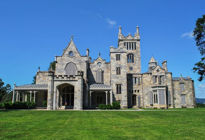 Historic home with Gothic architectural features and stone facade under a clear blue sky in a spacious green lawn setting.