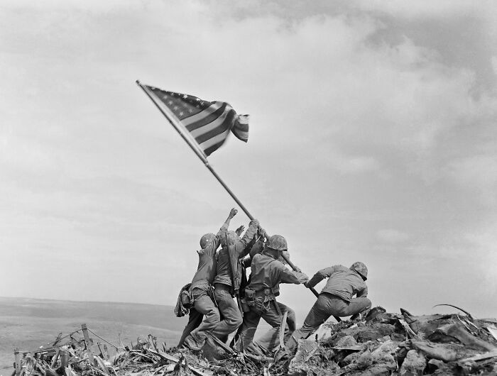 Soldiers raising the American flag on a battlefield, a somber photo from history capturing a powerful moment.