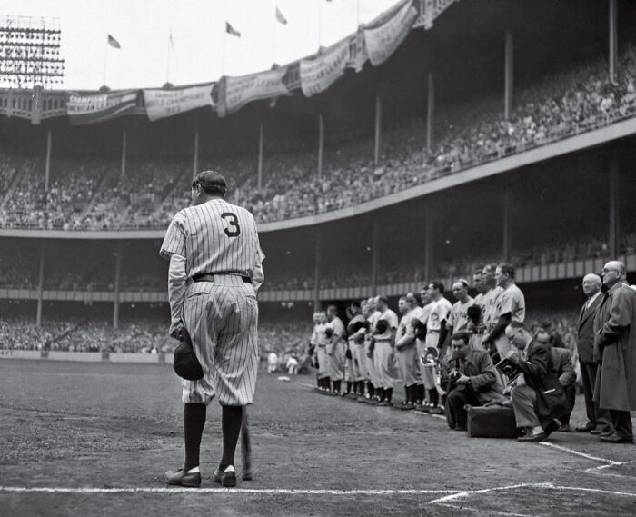 Baseball player standing alone on the field in front of a lined-up team during a somber historic moment.