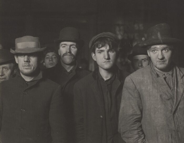 Group of somber men wearing hats and coats in a historical setting, capturing a gut-wrenching story from history.