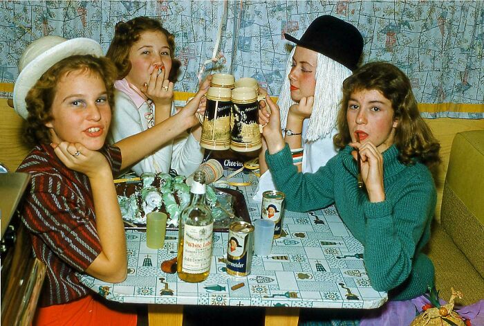 Four teenagers in vintage clothing enjoying drinks and snacks, capturing candid glimpses into the past.
