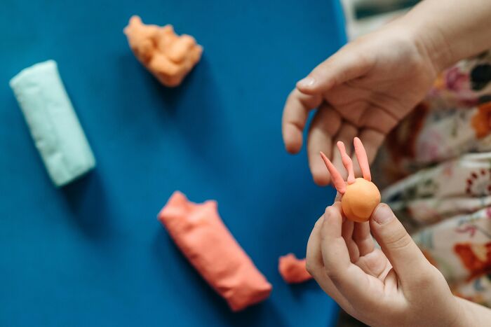 Child molding orange clay with multiple clay bars nearby, showing creative use of ingenious inventions over time.