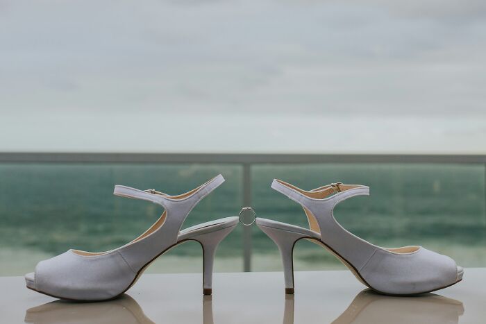 Pair of elegant white high-heeled shoes balanced with a wedding ring, showcasing ingenious inventions repurposed over the years.
